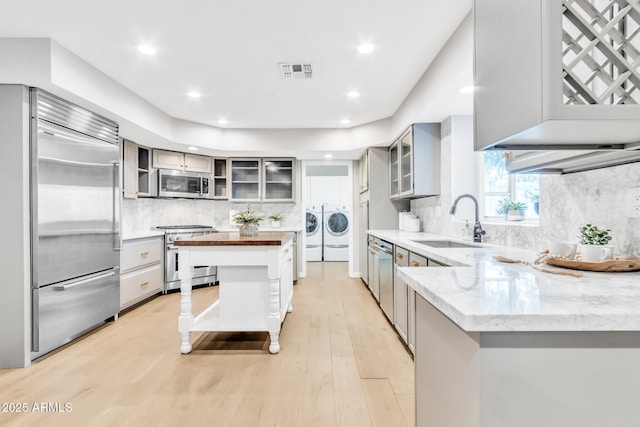 kitchen with high quality appliances, butcher block counters, decorative backsplash, washing machine and clothes dryer, and sink