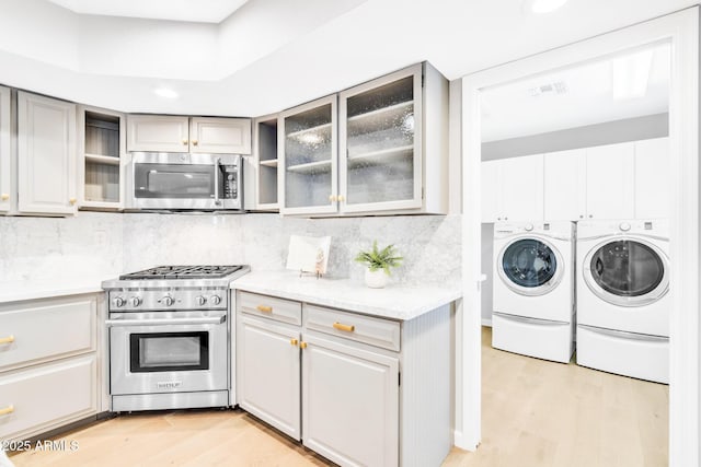 kitchen with appliances with stainless steel finishes, washing machine and clothes dryer, gray cabinets, and decorative backsplash