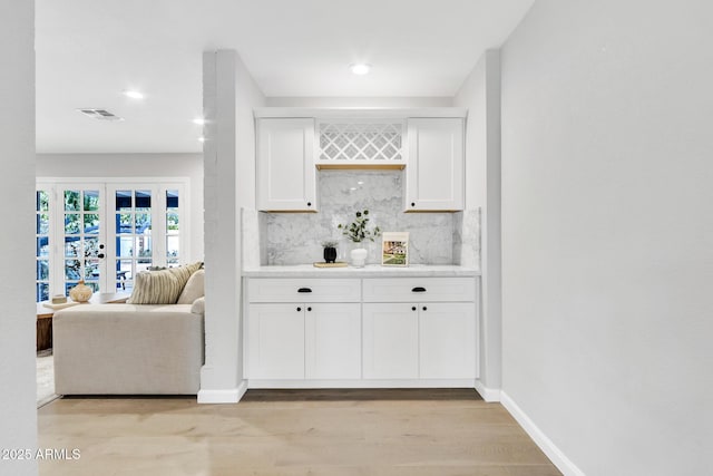 bar with french doors, white cabinets, tasteful backsplash, and light hardwood / wood-style flooring