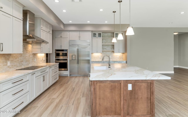 kitchen featuring light wood-type flooring, decorative backsplash, stainless steel appliances, wall chimney exhaust hood, and a sink