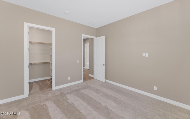 unfurnished bedroom featuring a closet, a walk in closet, baseboards, and carpet floors