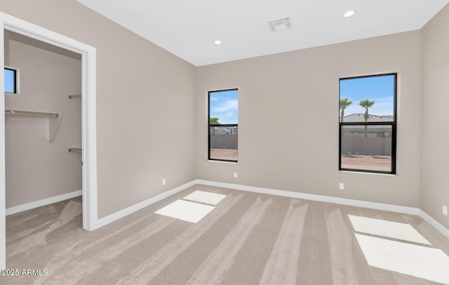 unfurnished bedroom featuring light carpet, visible vents, a spacious closet, and baseboards