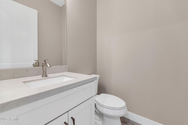 half bath featuring vanity, toilet, and baseboards