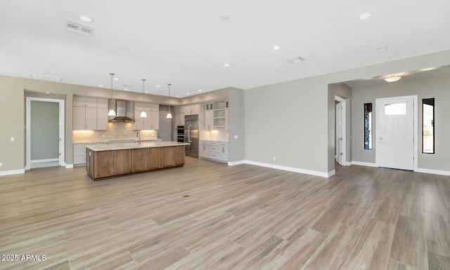 kitchen featuring visible vents, light countertops, wall chimney exhaust hood, open floor plan, and backsplash