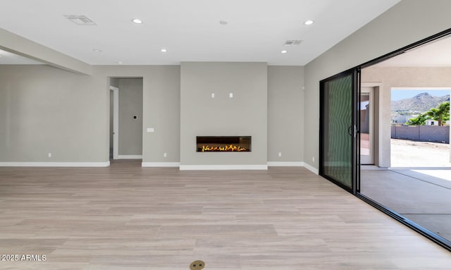 unfurnished living room with visible vents, recessed lighting, light wood-style floors, and a glass covered fireplace