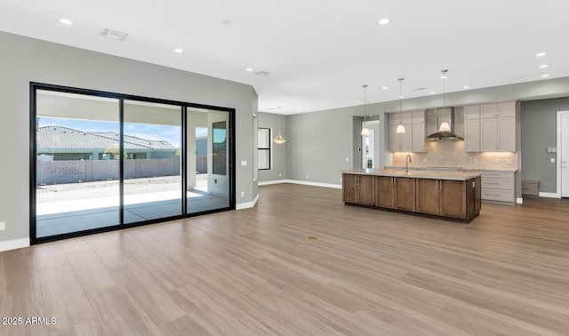 kitchen featuring light countertops, light wood-style floors, wall chimney range hood, open floor plan, and backsplash