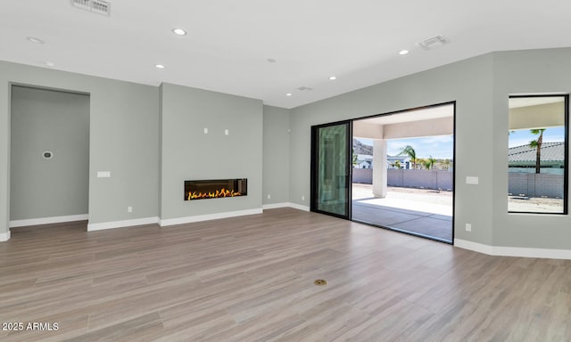 unfurnished living room with visible vents, baseboards, light wood-style flooring, recessed lighting, and a glass covered fireplace