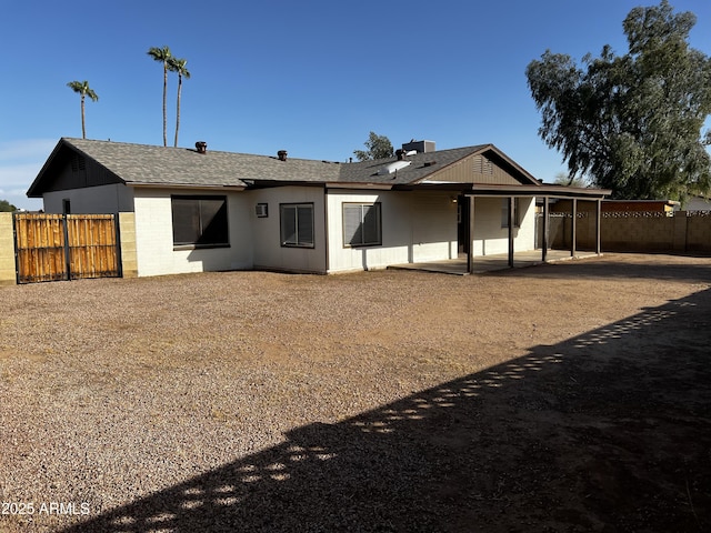 rear view of property with concrete block siding, a patio area, fence, and a shingled roof