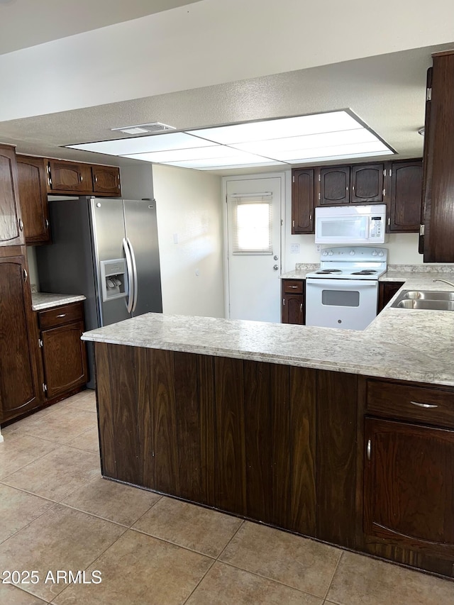 kitchen featuring white appliances, a peninsula, light tile patterned flooring, a sink, and dark brown cabinets