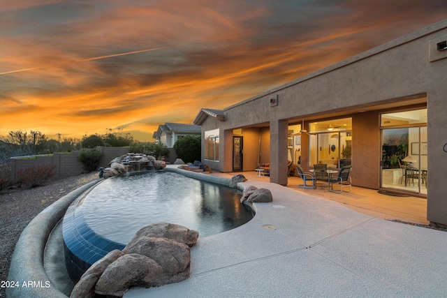 pool at dusk featuring pool water feature and a patio