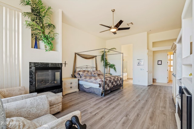 bedroom featuring ceiling fan, a high end fireplace, and light hardwood / wood-style flooring