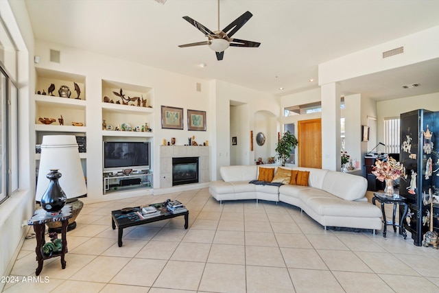 living room featuring ceiling fan, light tile patterned floors, built in features, and a fireplace