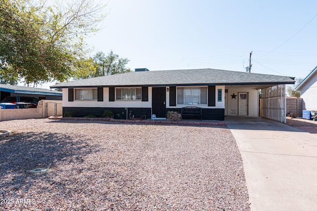 ranch-style home with a carport, a shingled roof, concrete driveway, and fence