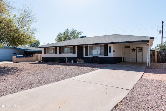 ranch-style home featuring driveway, an attached carport, roof with shingles, and fence