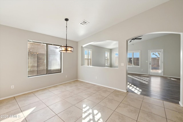empty room featuring a wealth of natural light, light tile patterned flooring, lofted ceiling, and ceiling fan with notable chandelier