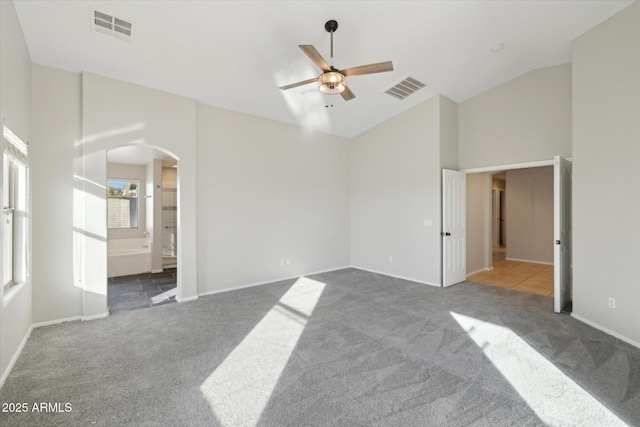 interior space featuring vaulted ceiling, ceiling fan, dark carpet, and ensuite bath