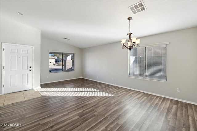 empty room featuring lofted ceiling, a notable chandelier, and hardwood / wood-style flooring