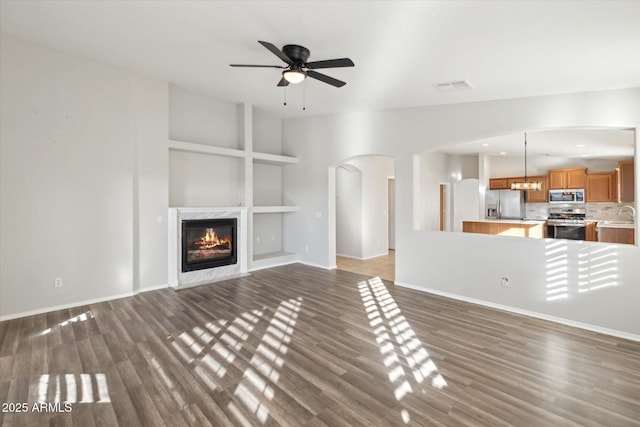 unfurnished living room with a premium fireplace, ceiling fan, dark wood-type flooring, and sink