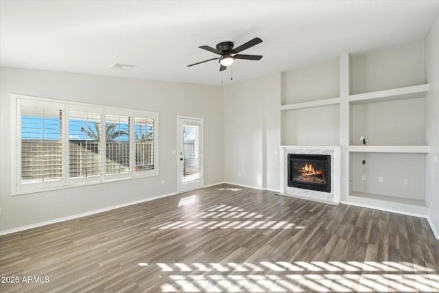 unfurnished living room featuring dark wood-type flooring, ceiling fan, a fireplace, and built in shelves