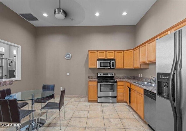 kitchen with sink, stainless steel appliances, a high ceiling, light stone counters, and light tile patterned floors