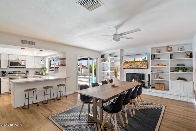 6271 E Evans Dr, Scottsdale, AZ 85254 - dining space featuring a large fireplace, visible vents, light wood-type flooring, and a textured ceiling