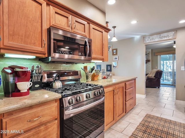 kitchen featuring pendant lighting, appliances with stainless steel finishes, backsplash, light stone counters, and light tile patterned flooring