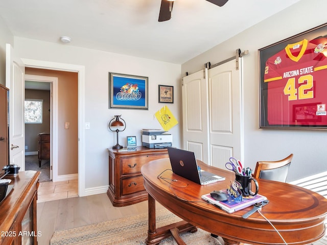 office with light hardwood / wood-style floors, a barn door, and ceiling fan