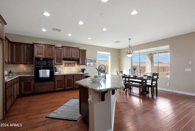 kitchen featuring an island with sink, dark hardwood / wood-style floors, black appliances, pendant lighting, and sink