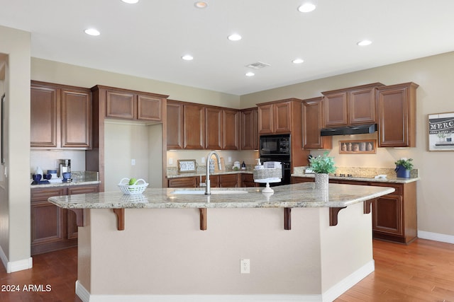 kitchen with light stone counters, a kitchen island with sink, and a kitchen bar