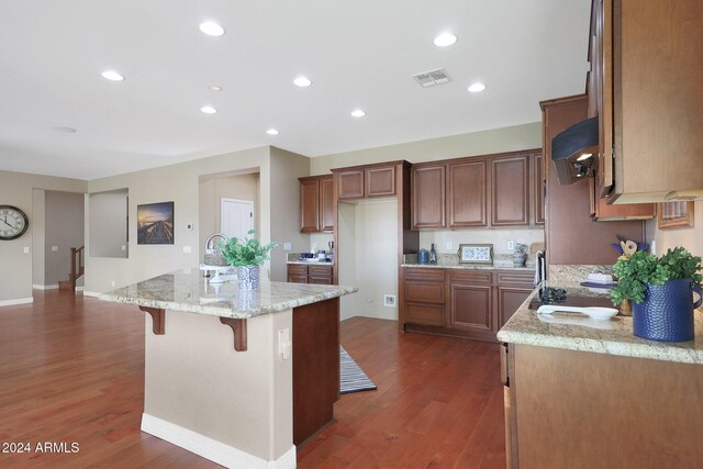 kitchen with visible vents, dark wood-style flooring, a center island with sink, and light stone countertops