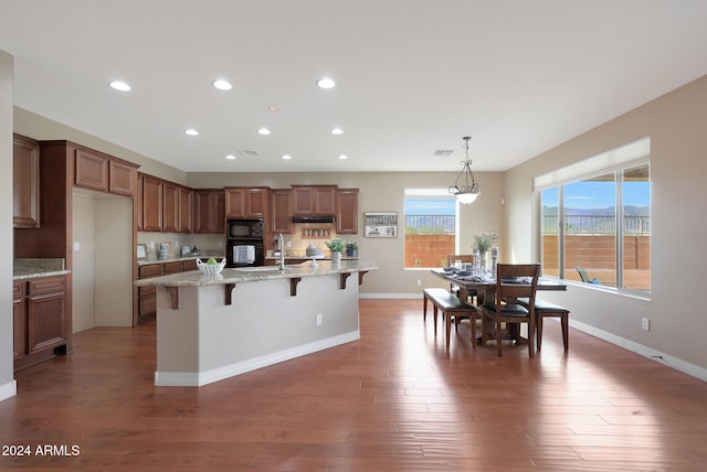 kitchen with a breakfast bar area, brown cabinetry, recessed lighting, wood finished floors, and black appliances