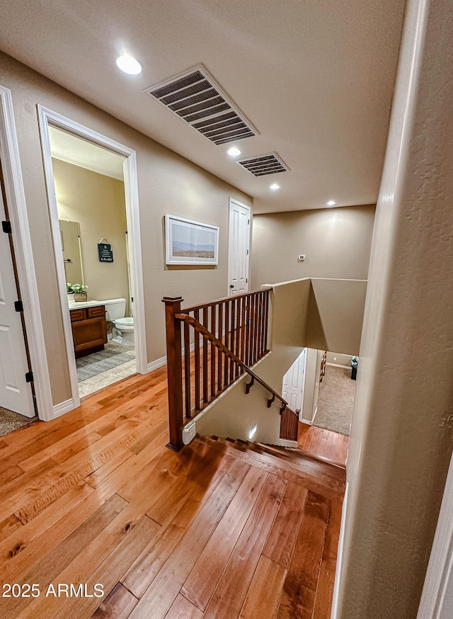 hall featuring visible vents, light wood-style flooring, baseboards, and an upstairs landing