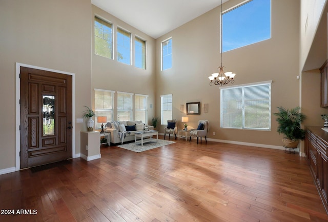 living area with wood-type flooring, baseboards, an inviting chandelier, and a towering ceiling