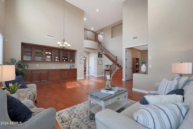 living area featuring an inviting chandelier, wood finished floors, visible vents, and a towering ceiling