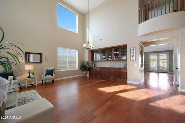 living area featuring an inviting chandelier, visible vents, wood finished floors, baseboards, and high vaulted ceiling