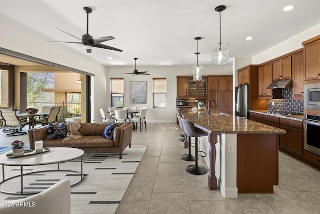 kitchen featuring stainless steel appliances, tasteful backsplash, a sink, under cabinet range hood, and a kitchen breakfast bar