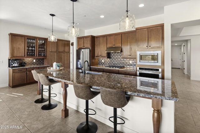 kitchen with under cabinet range hood, a breakfast bar, a sink, appliances with stainless steel finishes, and tasteful backsplash