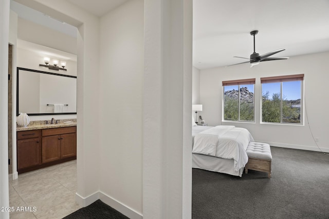 bedroom featuring light colored carpet, a sink, ensuite bath, and baseboards