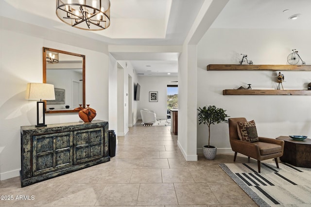 hall featuring a chandelier, a tray ceiling, baseboards, and tile patterned floors