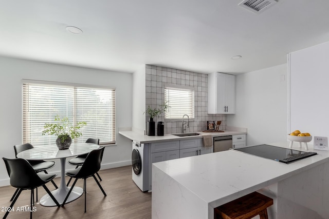 kitchen with backsplash, stainless steel dishwasher, sink, white cabinets, and washer / clothes dryer