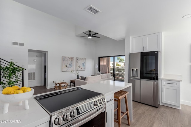 kitchen with light wood-type flooring, stainless steel appliances, ceiling fan, white cabinets, and a breakfast bar area