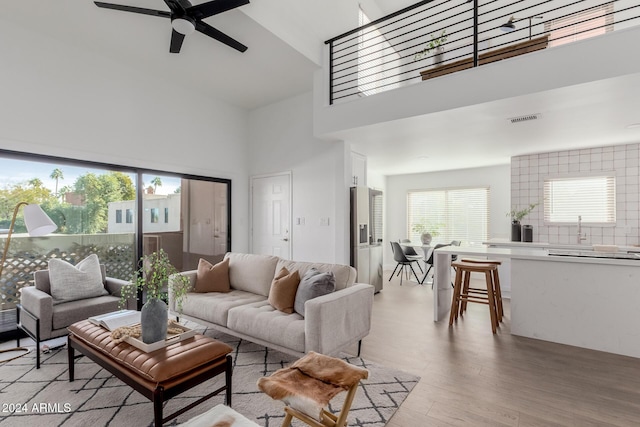 living room featuring ceiling fan, sink, a high ceiling, and light hardwood / wood-style flooring