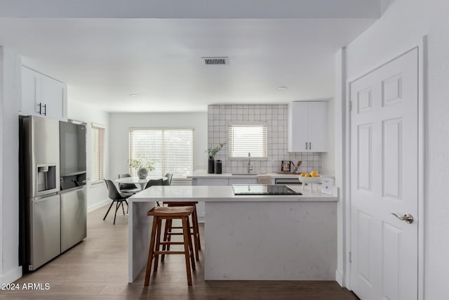 kitchen with stainless steel fridge with ice dispenser, white cabinetry, kitchen peninsula, and a breakfast bar area