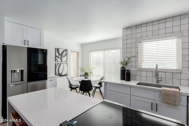 kitchen featuring backsplash, sink, stainless steel fridge, a wealth of natural light, and white cabinetry