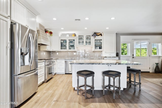 kitchen with light wood-type flooring, light stone counters, stainless steel appliances, and white cabinets