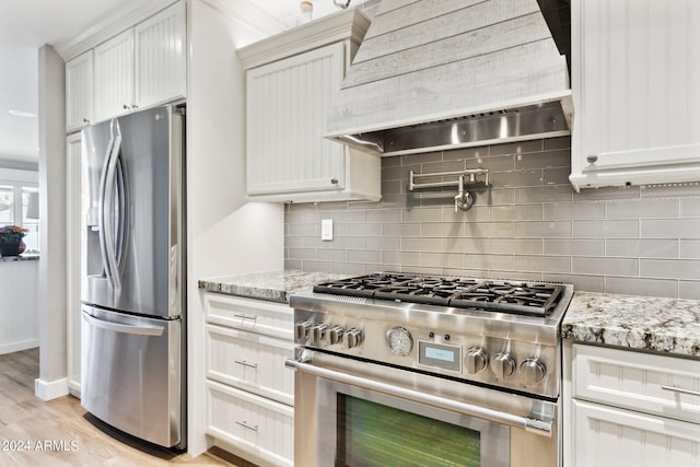 kitchen with light stone counters, premium range hood, backsplash, stainless steel appliances, and light wood-type flooring