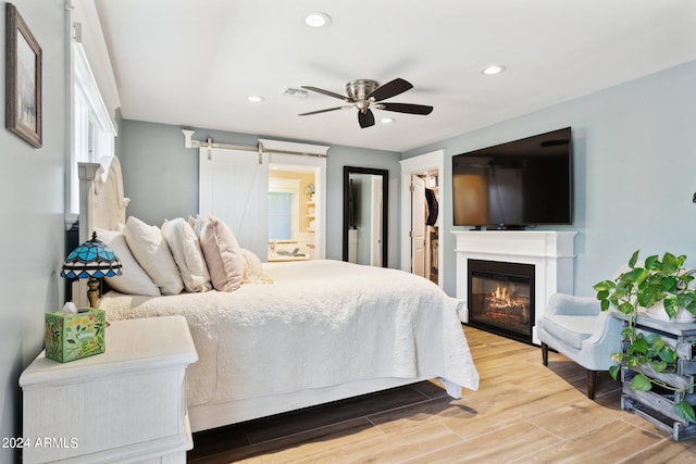 bedroom with ceiling fan, a walk in closet, hardwood / wood-style flooring, a closet, and a barn door