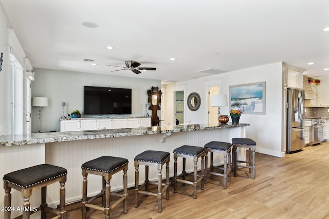 kitchen featuring light stone counters, stainless steel appliances, kitchen peninsula, and light hardwood / wood-style flooring