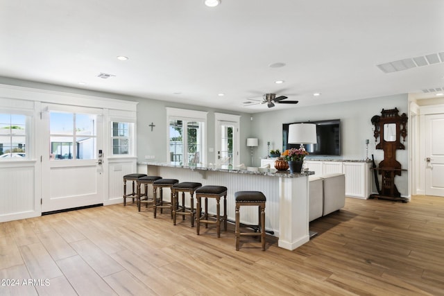 kitchen with a kitchen breakfast bar, white cabinets, light stone countertops, ceiling fan, and light hardwood / wood-style flooring