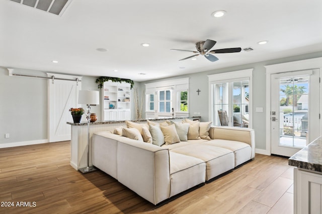 living room featuring ceiling fan, light wood-type flooring, a barn door, and a wealth of natural light